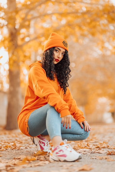 During the day, an orange hoodie and a blue denim jeans women sitting on the ground
